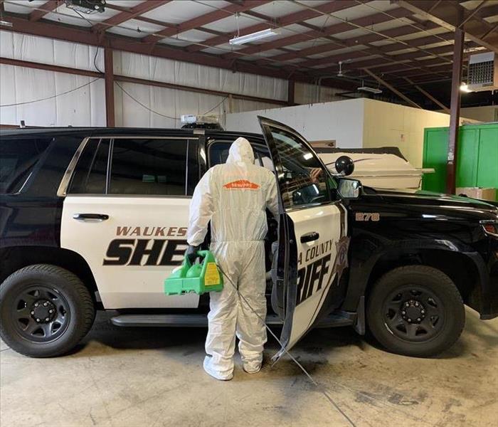 SERVPRO Employee Spraying Disinfectant in a Sheriff's Vehicle