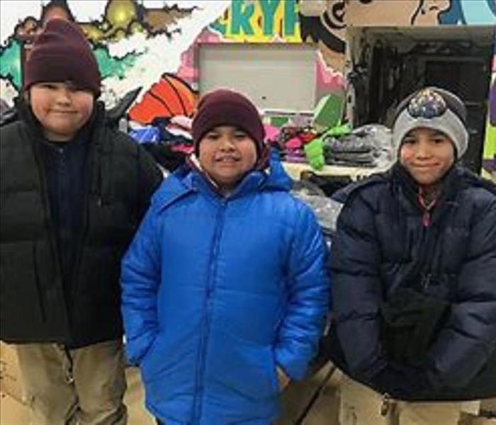 An image of three children in winter coats and hats from a clothing drive