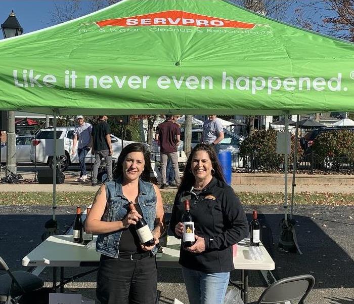 Two SERVPRO employees standing under a SERVPRO pop up tent holding bottles of wine