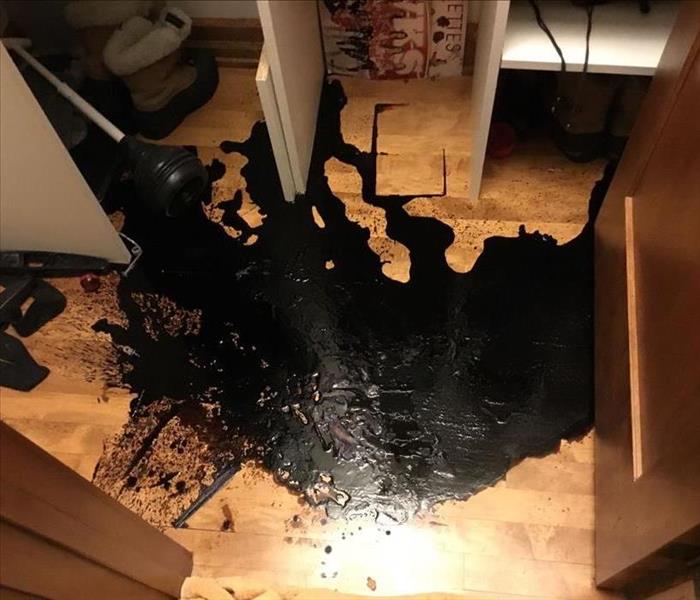Black chemical spilled on the hardwood floor in a closet
