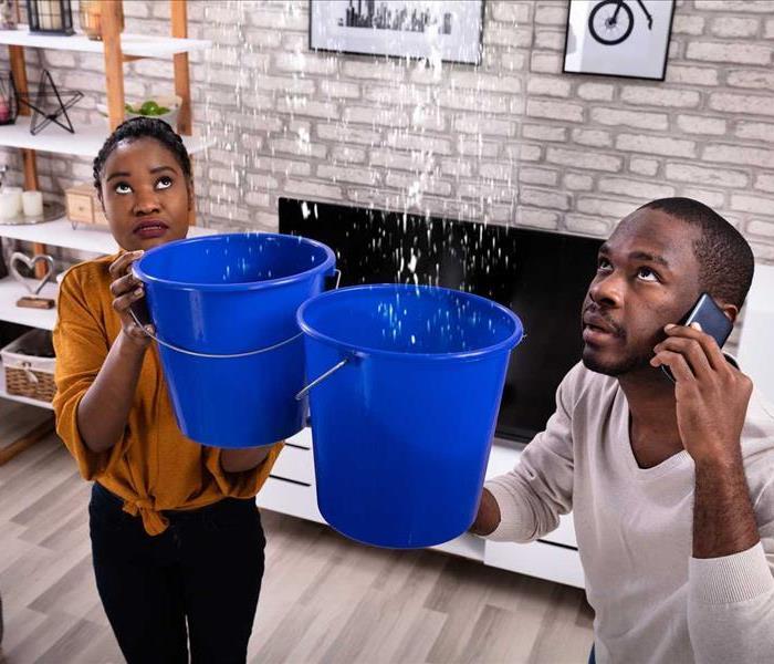 picture of 2 people holding buckets while water pours from the ceiling